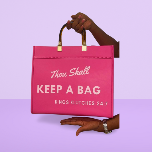 A pink faux leather tote bag with the text 'Thou Shall Keep A Bag' printed on the front, held by a model.